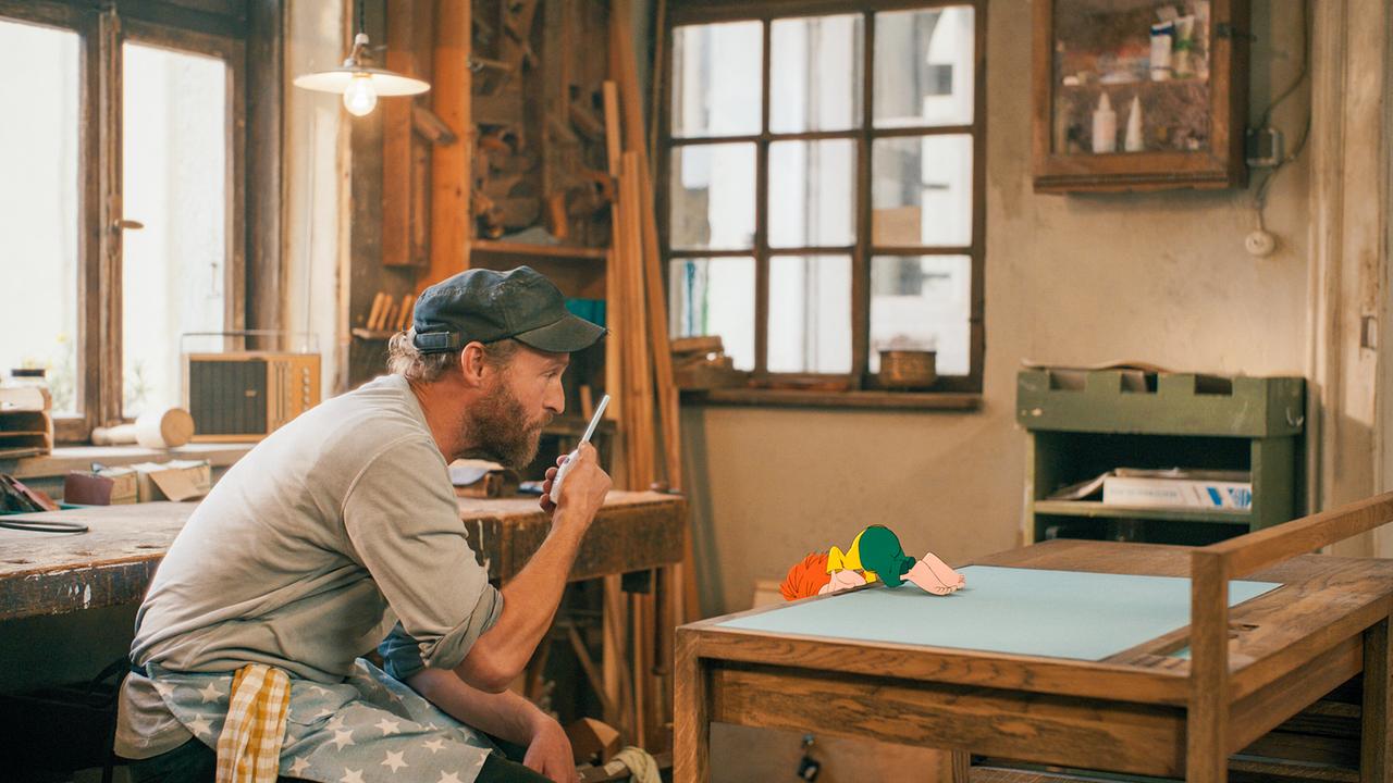 Tischlermeister Eder und Pumuckl suchen etwas in der Tischlerwerkstatt.