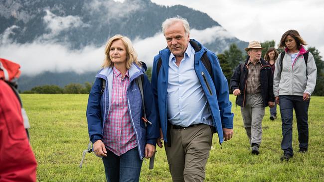 Christa, Helmut, Harry, Hilde und Miriam machen erneut eine Trauerreise und gehen dabei über eine grüne Wiese vor einer nebelverhangenen Berglandschaft.