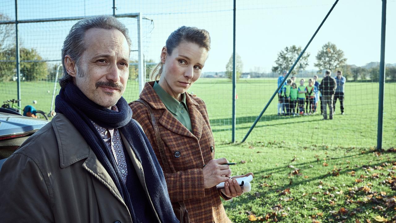 © ORF/ARD Degeto Film/BR/Hager Moss Film GmbH/Bernd Schuller Ferdinand Zankl wird von Kriminalhauptkommissarin Hermine Grill am Fußballplatz befragt.