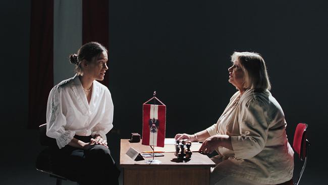 © ORF/April April Filme Antragstellerin und Beamtin, dazwischen Schreibtisch mit Österreichwinpel, Unterlagen und Stempel