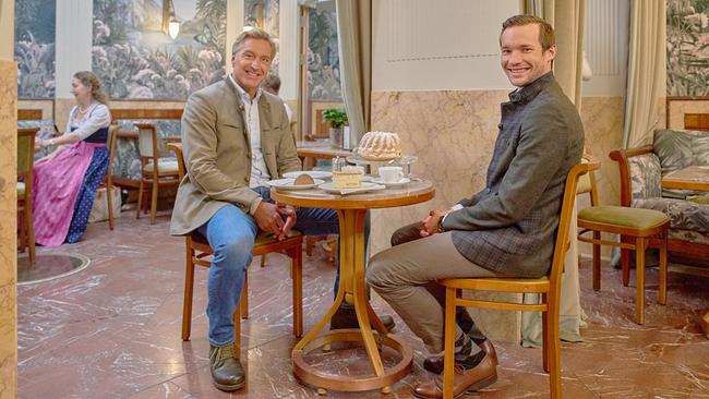 Hans Knauß sitzt mit Josef Zauner in einem stilvollen Café bei Kaffee, Torte und Gugelhupf, im Hintergrund eine Frau in Tracht.