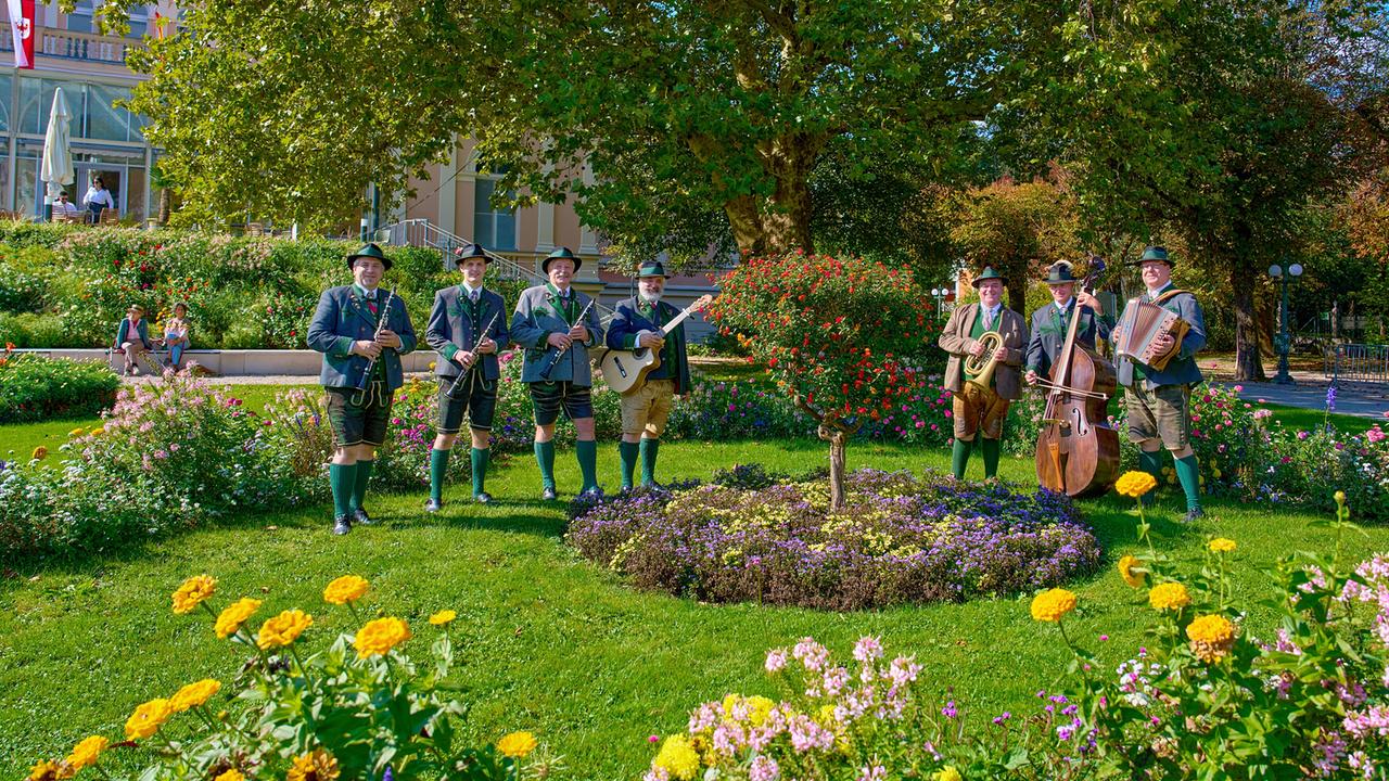 Die Pernecker Klarinettenmusi in einem gepflegten Park einer Kurstadt, umgeben von bunten Blumenbeeten.