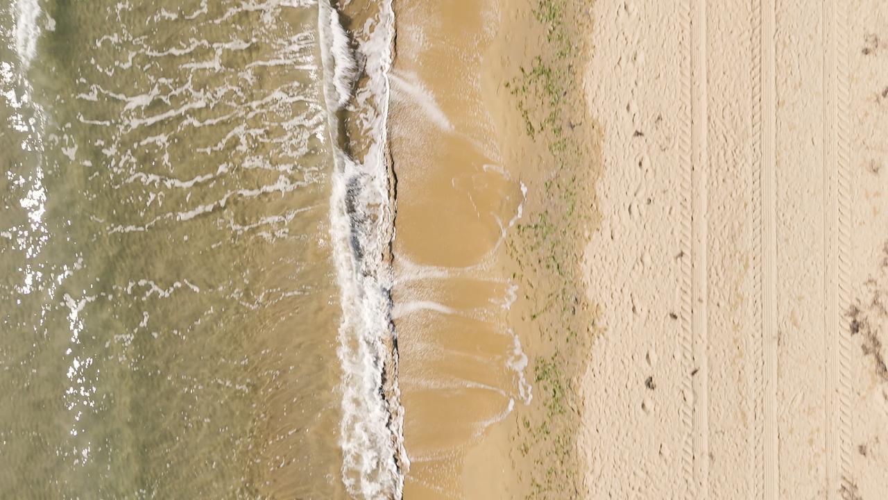 Flug über Strand von Lignano: Das Bild zeigt Wellen, die auf einen hellen Sandstrand treffen.