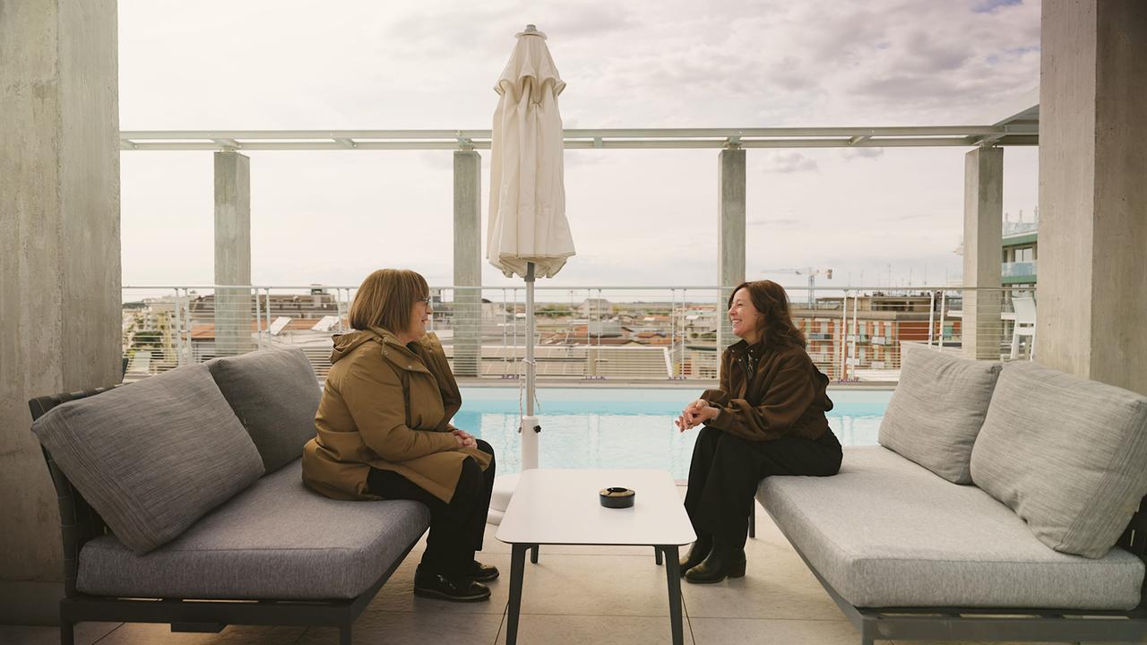 Julia Cencig im Gespräch mit Mariella D’Alloro (Hotelbesitzerin aus Caorle) auf einer modernen Dachterrasse mit Pool daneben