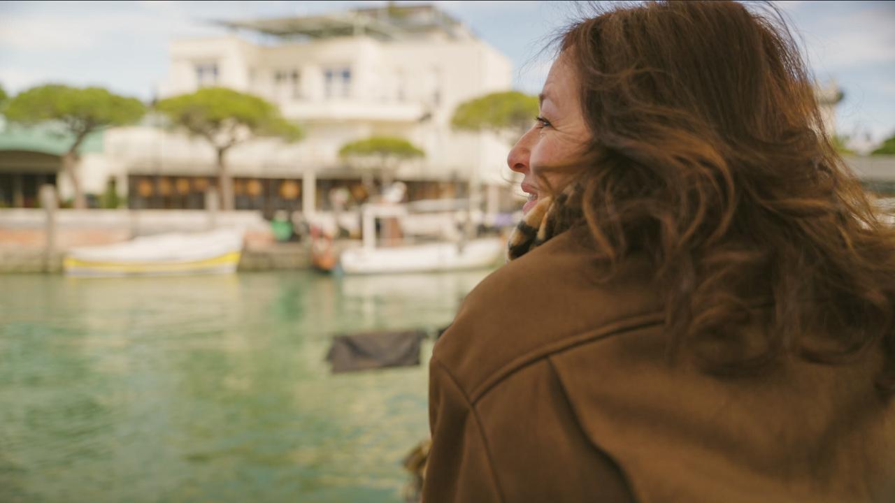 Julia Cencig blickt auf den Hafen von Caorle mit Booten und Gebäuden.