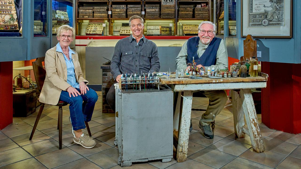 © ORF/Alois Kuschetz Hans Knauß sitzt mit Hannelore Handler-Woltran und Franz Rieder in einer Werkstatt mit Miniaturen, Farben und historischen Exponaten um einen Arbeitstisch.
