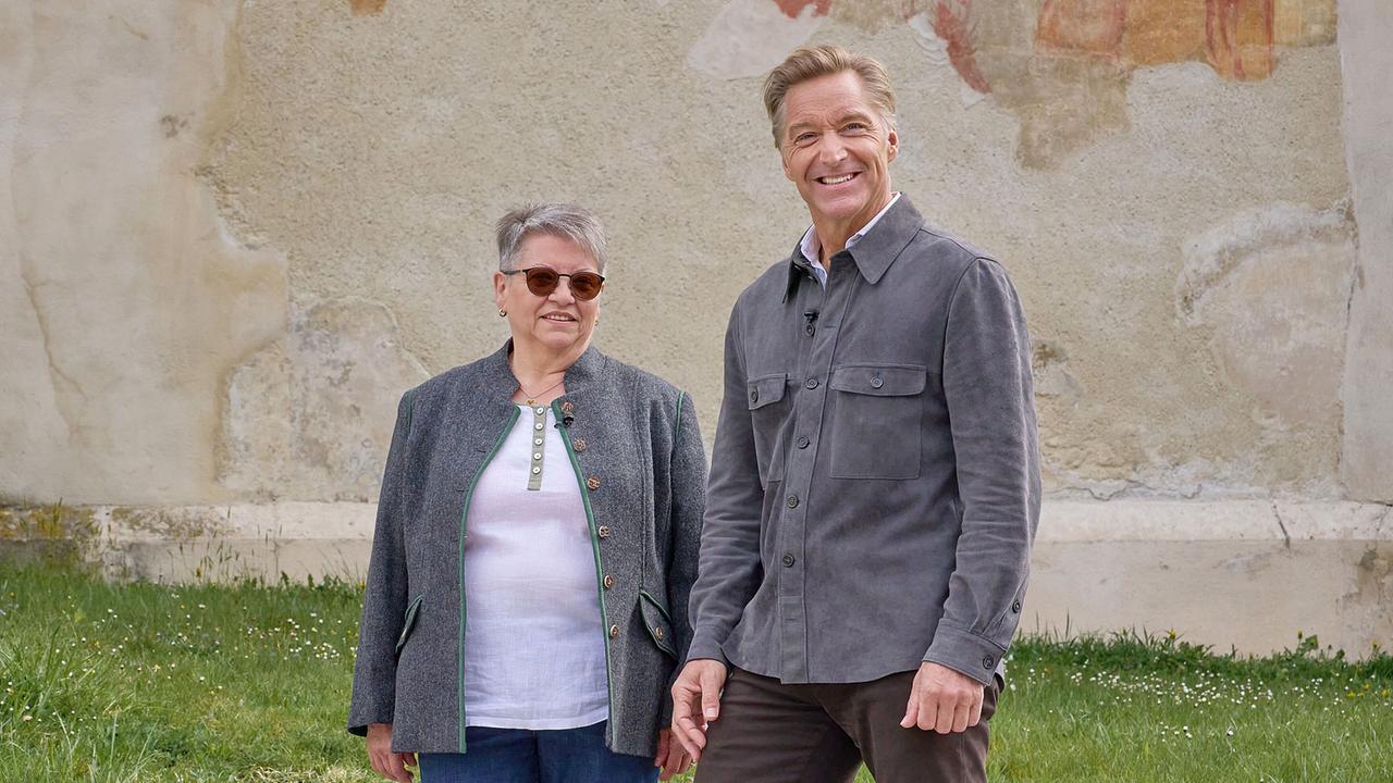 © ORF/Alois Kuschetz Hans Knauß und Ingrid Rieger stehen nebeneinander vor einer alten, bemalten Mauer auf einer Wiese.