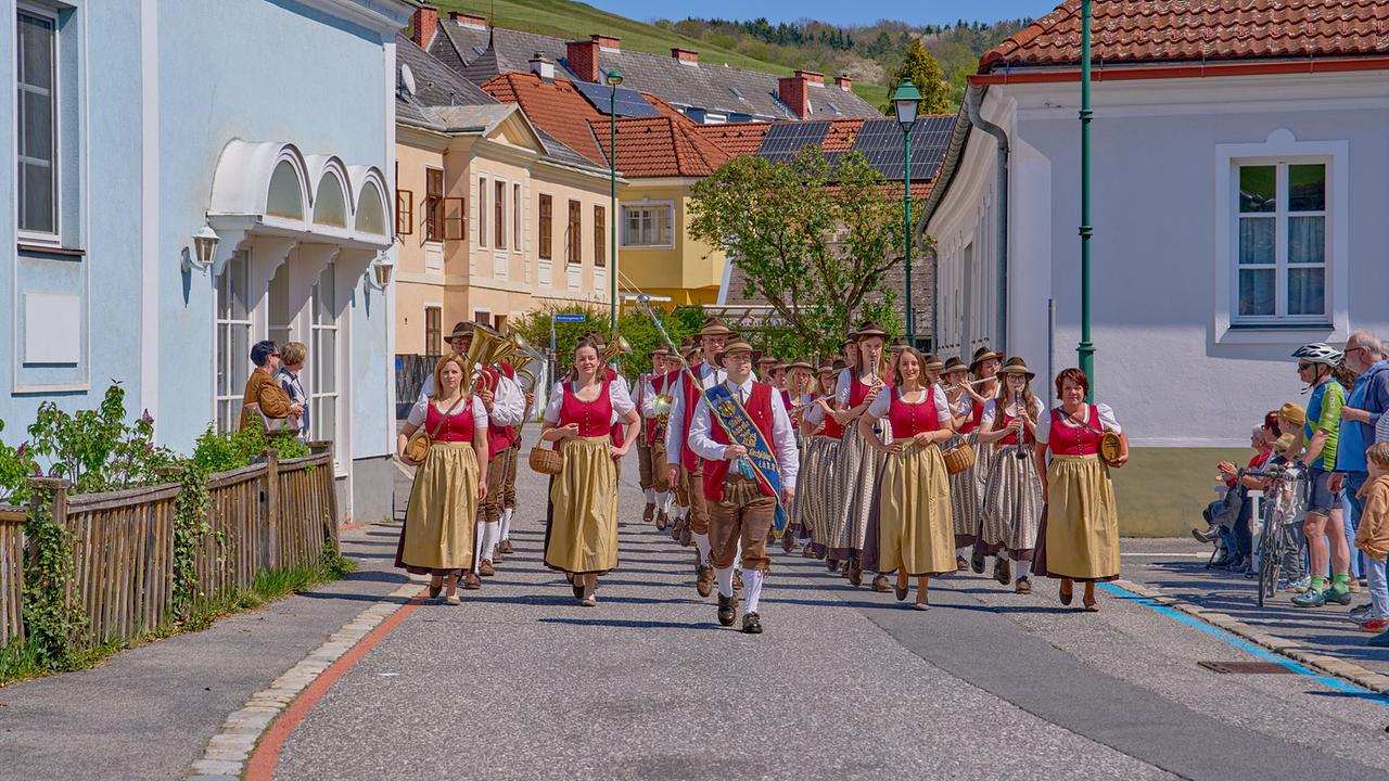 © ORF/Alois Kuschetz Die Stadtkapelle Kirchschlag zieht durch eine kleinstädtische Straße bei schönem Wetter.