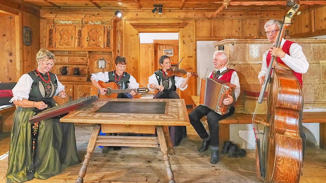 Die "Hausmusik Kraft" mit fünf Musiker:innen spielt in einer holzgetäfelten Stube Zither, Gitarre, Geige, Akkordeon und Kontrabass.