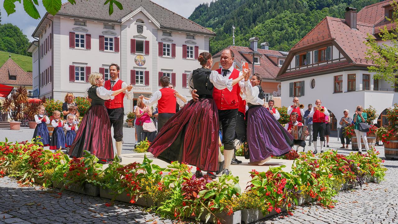 Die Trachtengruppe Schruns tanzt vor Publikum und Blasmusik auf dem Dorfplatz.