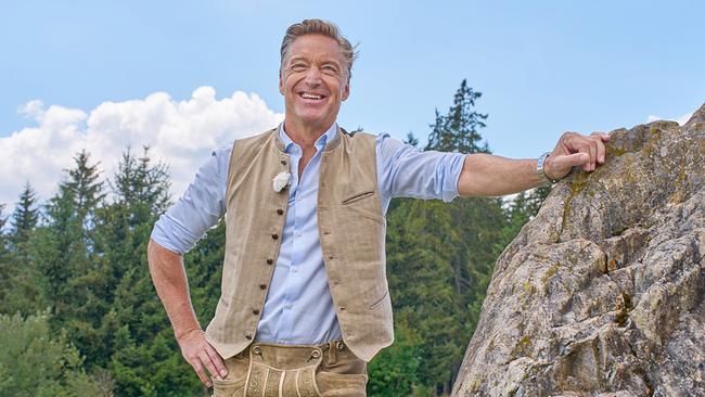 © ORF/Landesstudio Steiermark/Alois Kuschetz Hans Knauß stehtlächelnd neben einem großen Felsen vor einem Wald.
