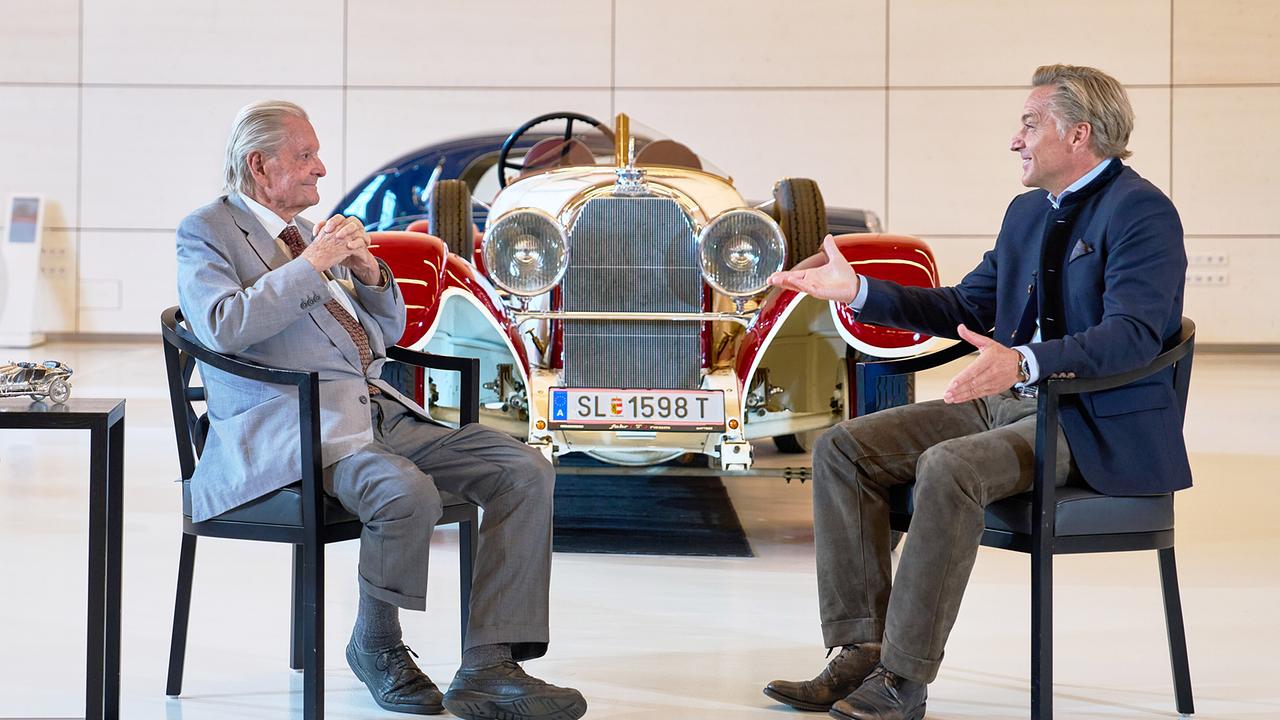 © ORF/Landesstudio Steiermark/Alois Kuschetz Hans Knauß spricht mit dem älteren Ernst Piech in einem hellen Raum vor einem prachtvollen historischen Oldtimer.