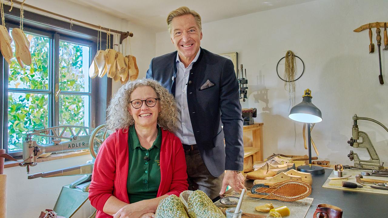 © ORF/Landesstudio Steiermark/Alois Kuschetz Hans Knauß steht hinter der Schuhmacherin Gerlinde Mackinger, die in ihrer Werkstatt geflochtene Schuhe zeigt.
