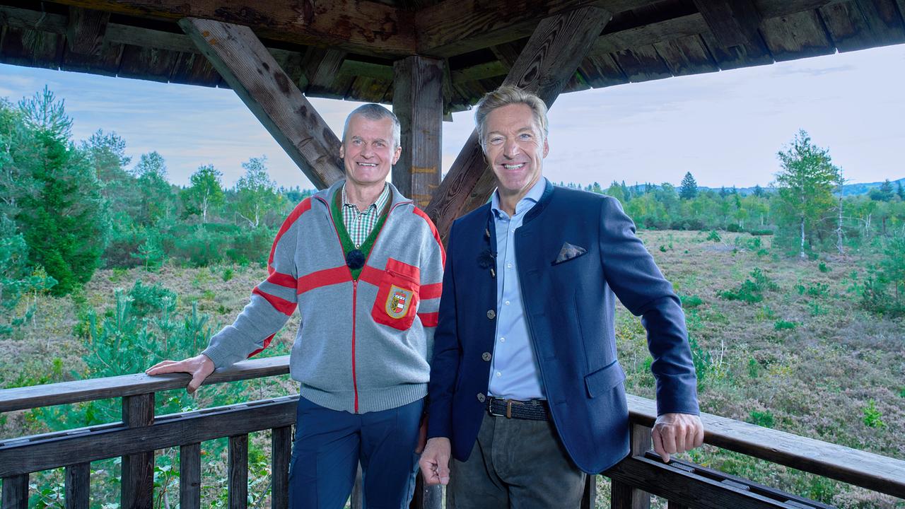 © ORF/Landesstudio Steiermark/Alois Kuschetz Josef Wengler und Hans Knauß stehen lächelnd auf einem hölzernen Aussichtsturm vor einer Waldlandschaft.