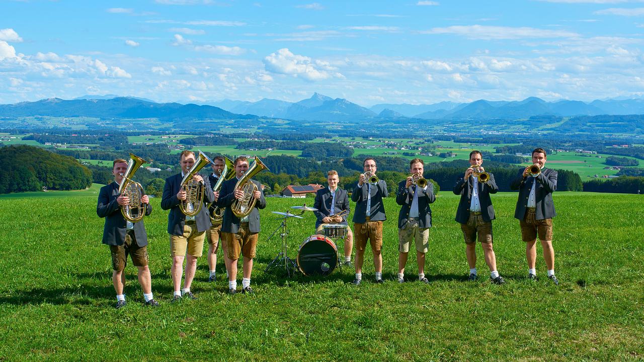 © ORF/Landesstudio Steiermark/Alois Kuschetz Die Wiesl Musi, neun Musiker, spielen mit ihren Blasinstrumenten und einem Schlagzeug auf einer Wiese vor einer weiten Hügellandschaft.