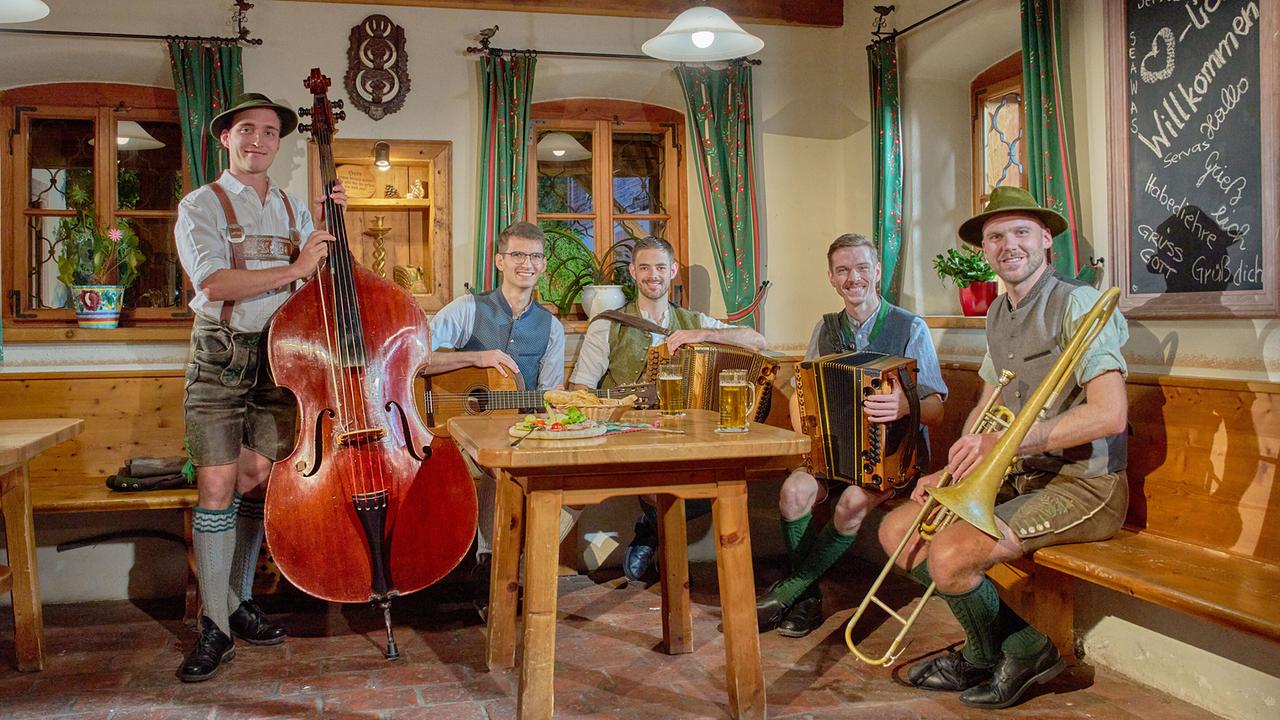 © ORF/Landesstudio Steiermark/Alois Kuschetz Die Schallmoser Buam, fünf Volksmusiker, sitzen mit ihren Instrumenten und zwei Biergläsern in einer gemütlichen Gaststube.