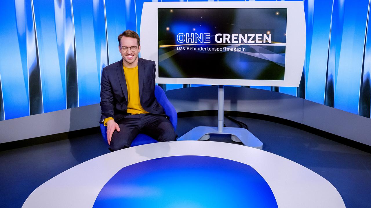 Andreas Onea im Studio mit großem Screen mit Schriftzug "OHNE GRENZEN - das Behindertensport Magazin" im Hintergrund