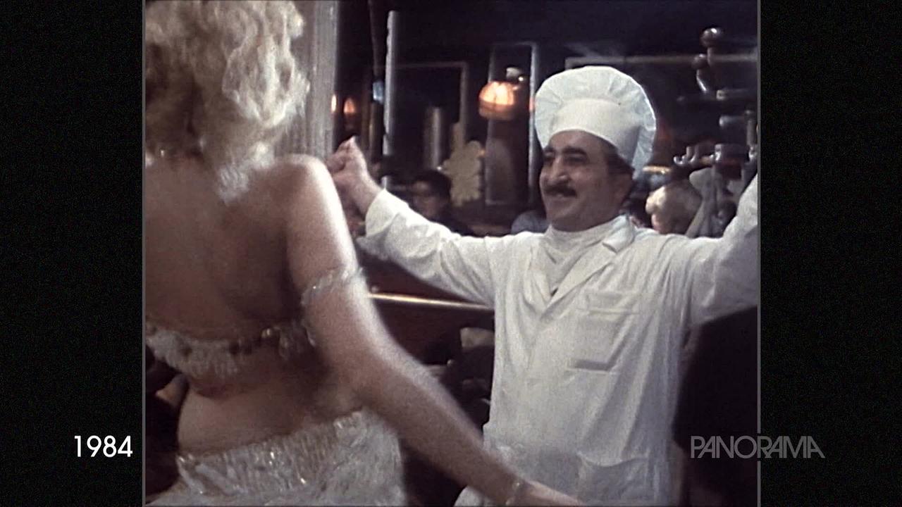 Am Bild aus dem Jahr 1984 ist eine Bauchtänzerin von hinten zu sehen, die gerade mit einem Koch in weißem Gewand und Kochmütze tanzt.