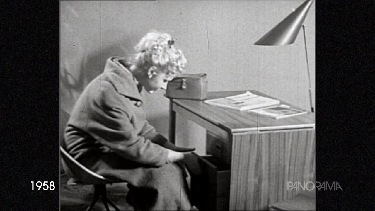 Am Bild aus dem Jahr 1958 ist eine junge blonde Dame, die an einem Schreibtisch sitzt und eine Lade öffnet.