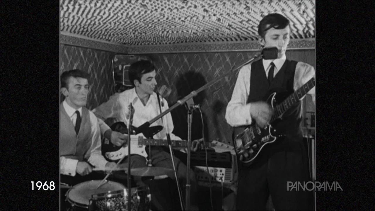 Auf dem schwarz-weiß-Foto aus dem Jahr 1968 sind drei junge Männer, die in einer Band spielen. Sie spielen E-Gitarren und Schlagzeug.