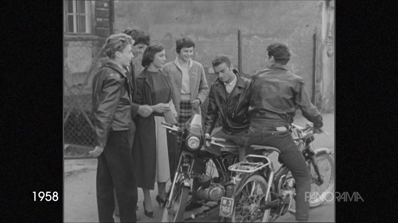 Am Bild aus dem Jahr 1958 ist eine Gruppe junger Leute zu sehen, die sich auf der Straße getroffen haben. Zwei junge Männer sitzen auf ihren Motorrädern.