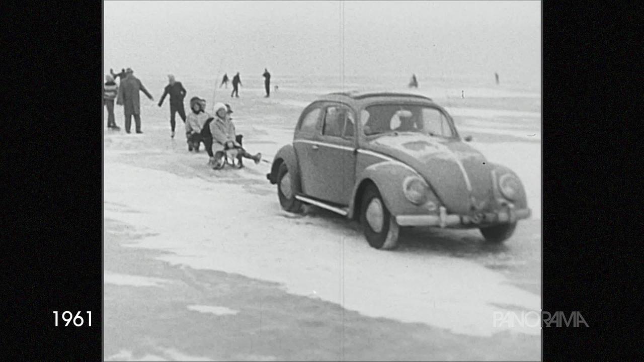 Am Bild aus dem Jahr 1961 ist ein VW-Käfer zu sehen, der auf einer zugefrorenen Eisdecke mehrere Personen zieht, die auf Schlitten sitzen.