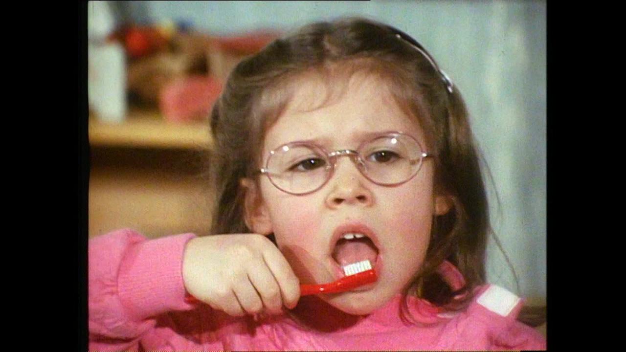 Am Bild ist ein kleines Mädchen mit Brille, die gerade Zähne putzt.