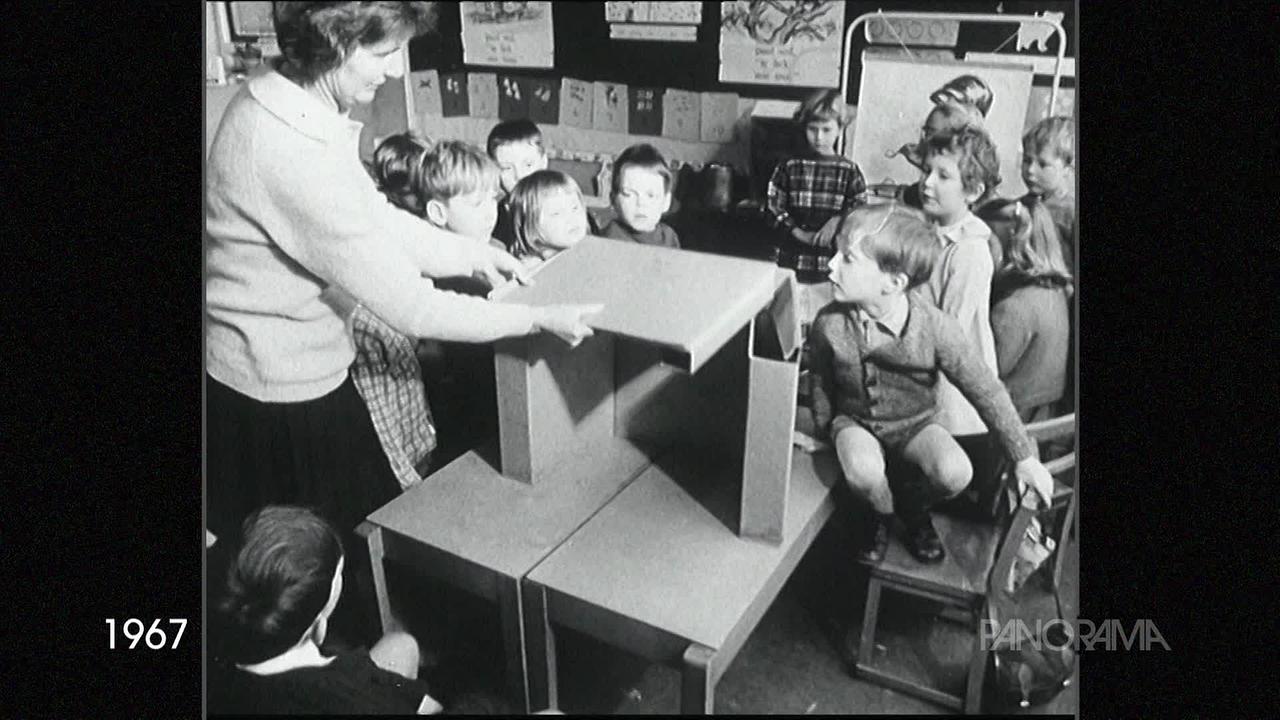 Am Schwarz-Weiss-Bild aus dem Jahr 1967 ist eine Schulklasse zu sehen mit ihrer Lehrerin. Sie basteln gerade aus Pappe Tische und Hocker zusammen.