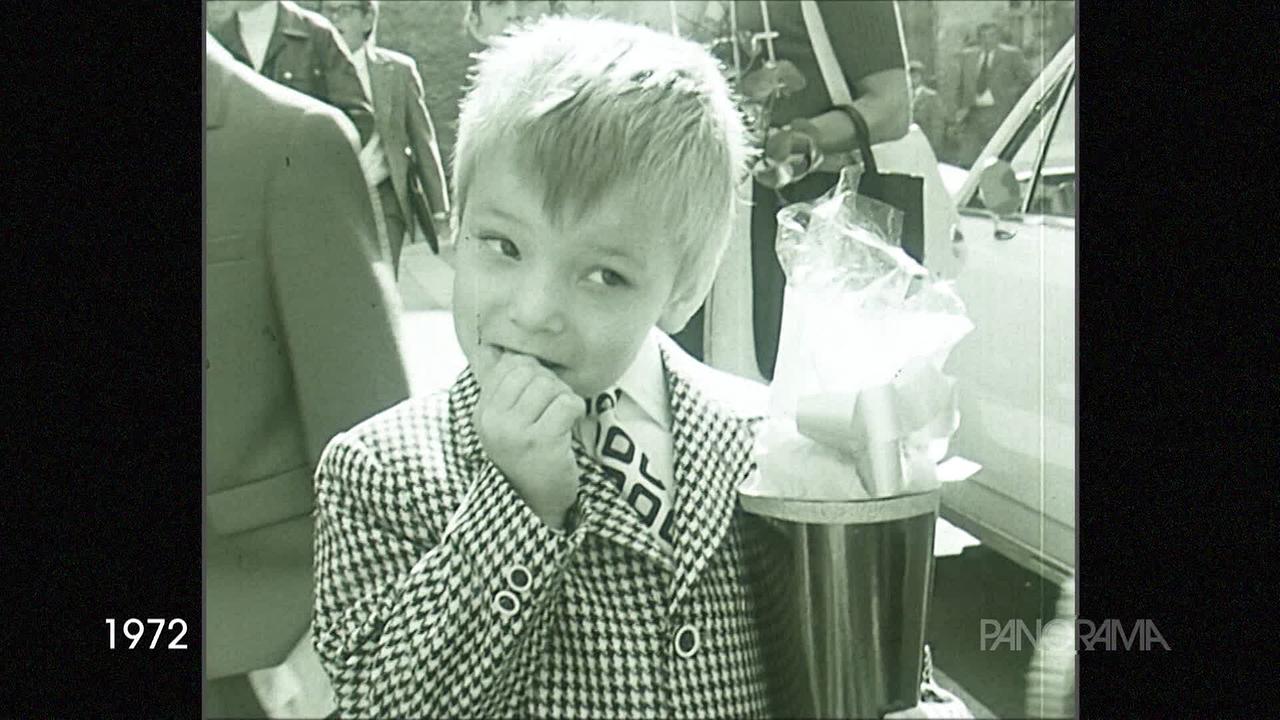 © ORF Am Bild aus dem Jahr 1972 ist ein blonder Bub, der ein Hemd, Krawatte und eine schwarz weiß gemusterte Jacke trägt. Er kaut auf deinen Nägeln und hat eine Schultüte in der Hand. Im Hintergrund sind viele Erwachsene zu sehen und ein Auto.