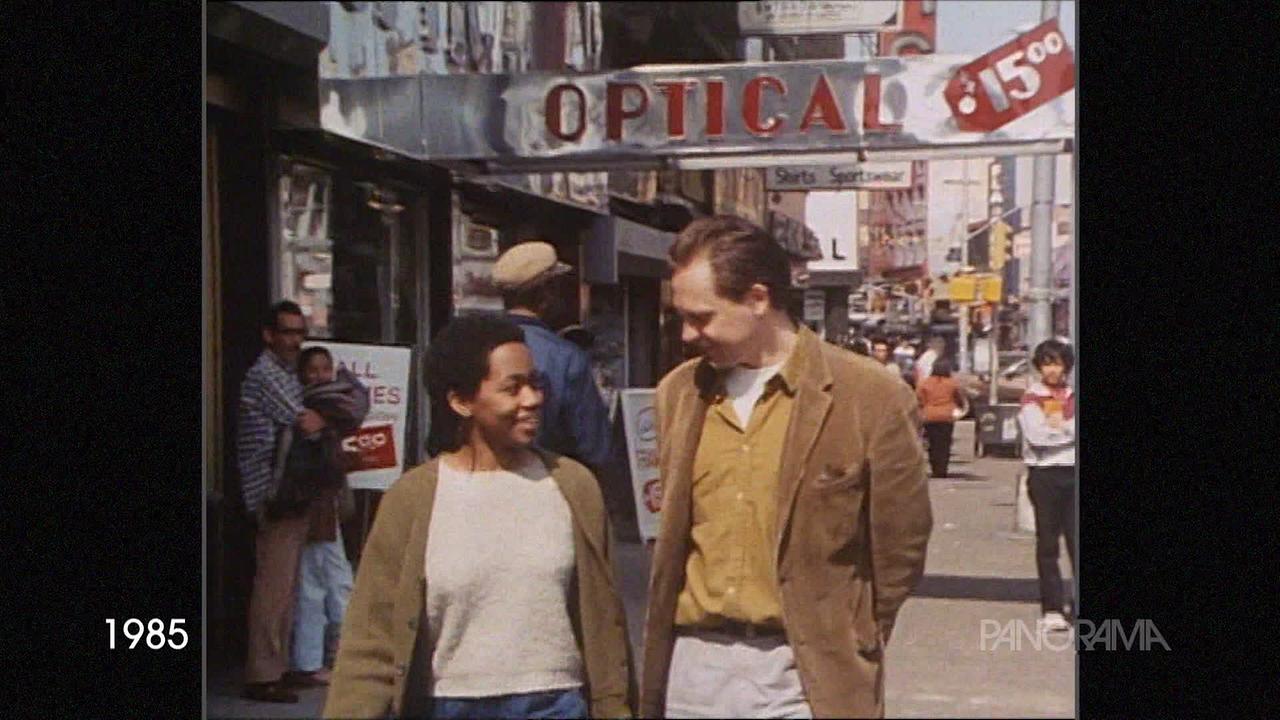 Auf dem Bild aus dem Jahr 1985 sind Menschen verschiedener Ethnien in einer belebten Straße von New York zu sehen. Im Vordergrund gehen eine schwarze Frau und ein weißer Mann miteinander spazieren.