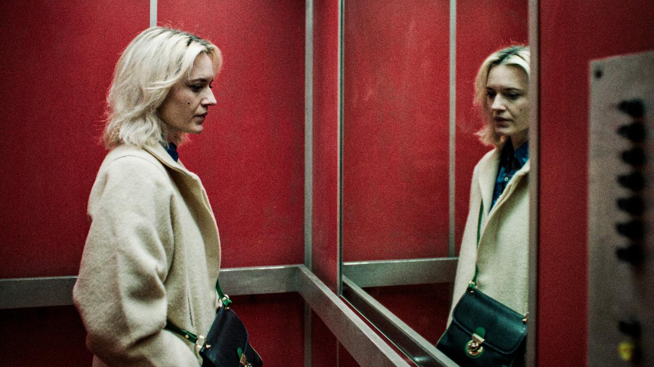 © ORF/Stadtkino Filmverleih/Golden Girls Film Perla steht ernst in einem rot verkleideten Aufzug vor einem Spiegel und schaut zu Boden.