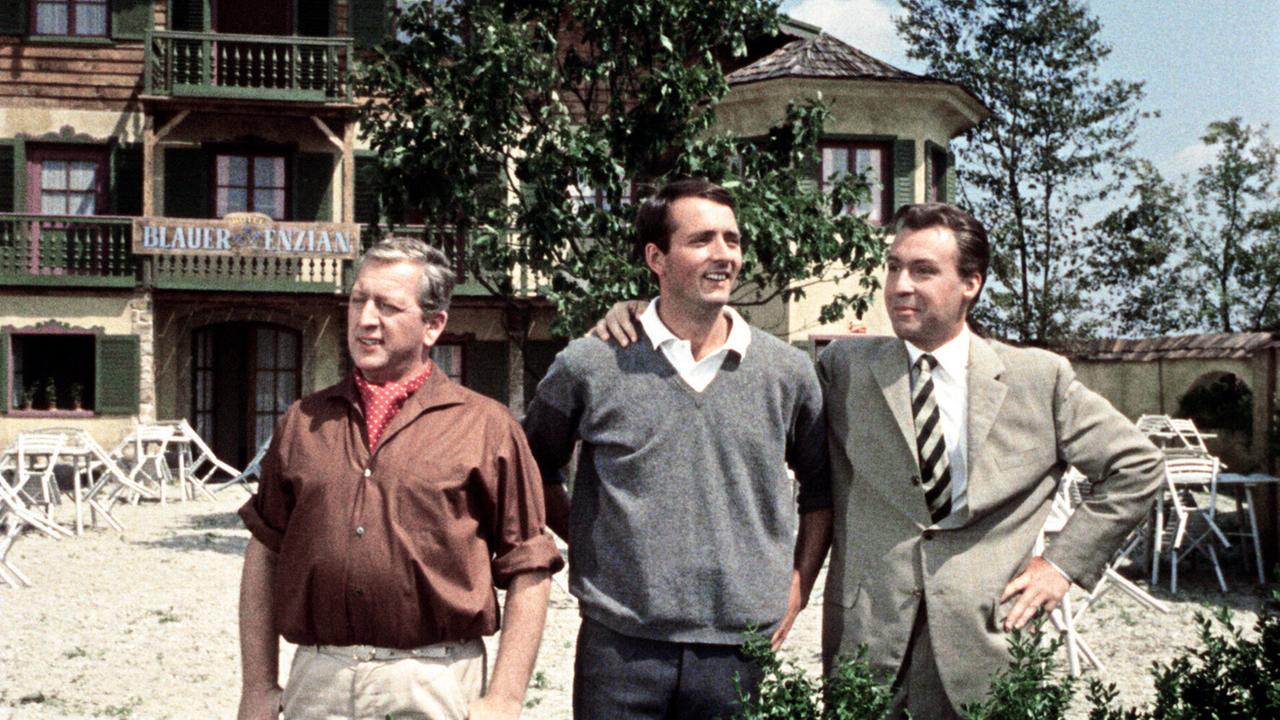 Im sonnigen Gastarten des Wirtshauses 'Blauer Enzian' stehen die drei Freunde Toni, Hans und Heinz nebeneinander