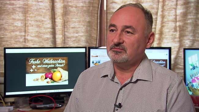 Gastronom Herr. B. sitzt beim Interview in einem Büro, im Hintergrund sind mehrere Monitore mit weihnachtlichen Motiven zu sehen.