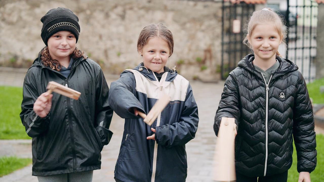 Drei lachende Ratschenkinder drehen ihre Holzratschen.