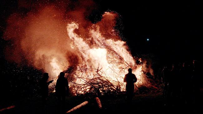Ein loderndes Osterfeuer bei Nacht mit mehreren Personen im Vordergrund.