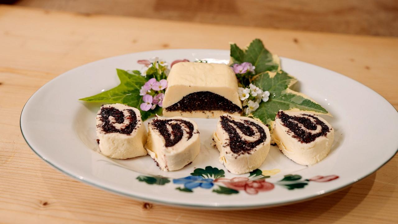 Gefüllte Mohnbutter in Scheiben und als Stück auf einem Teller mit Blättern und Blüten angerichtet