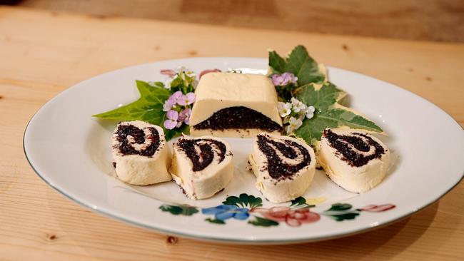 Gefüllte Mohnbutter in Scheiben und als Stück auf einem Teller mit Blättern und Blüten angerichtet
