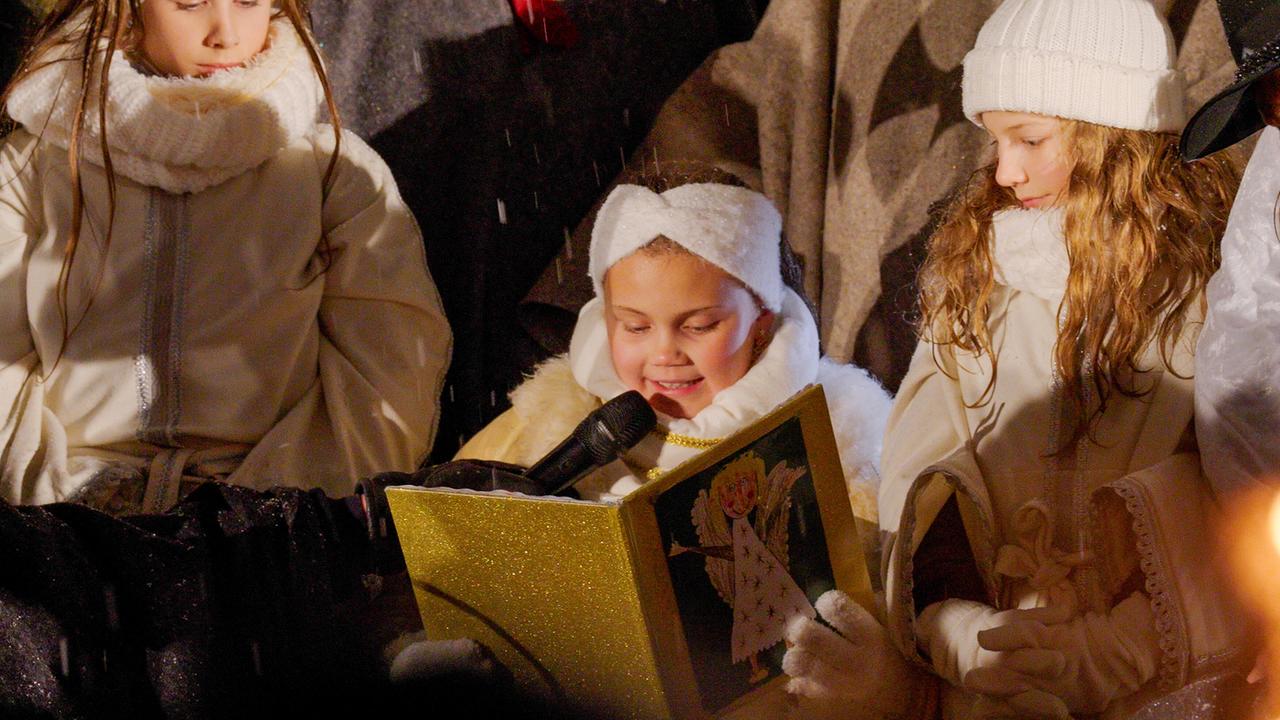 Drei Kinder in Engels-Kostümen, eines - das Christkind von Villach - liest aus einem Buch