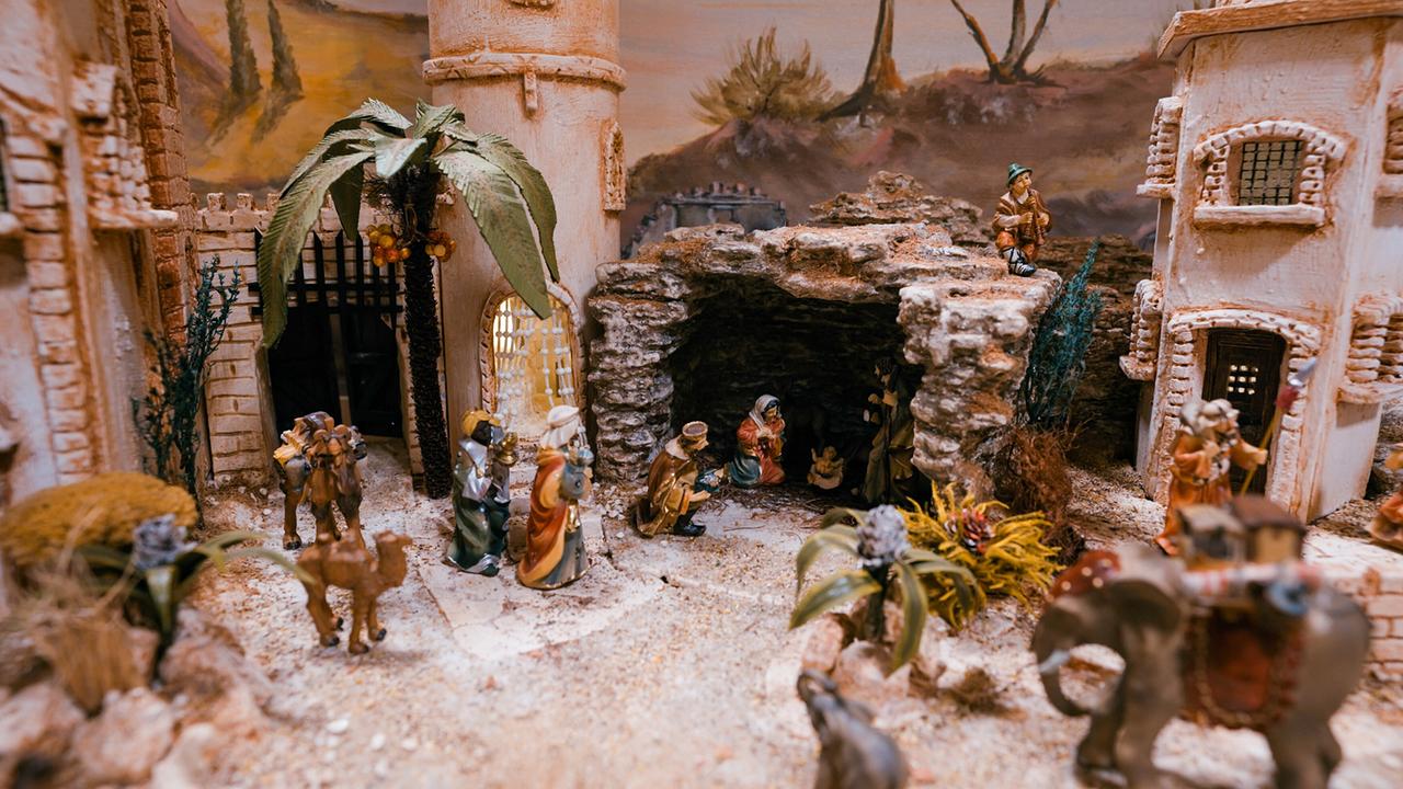 Orientalische Krippe mit Figuren in traditioneller Kleidung vor einer Felshöhle und mehreren Gebäuden bei der Villacher Krippenausstellung