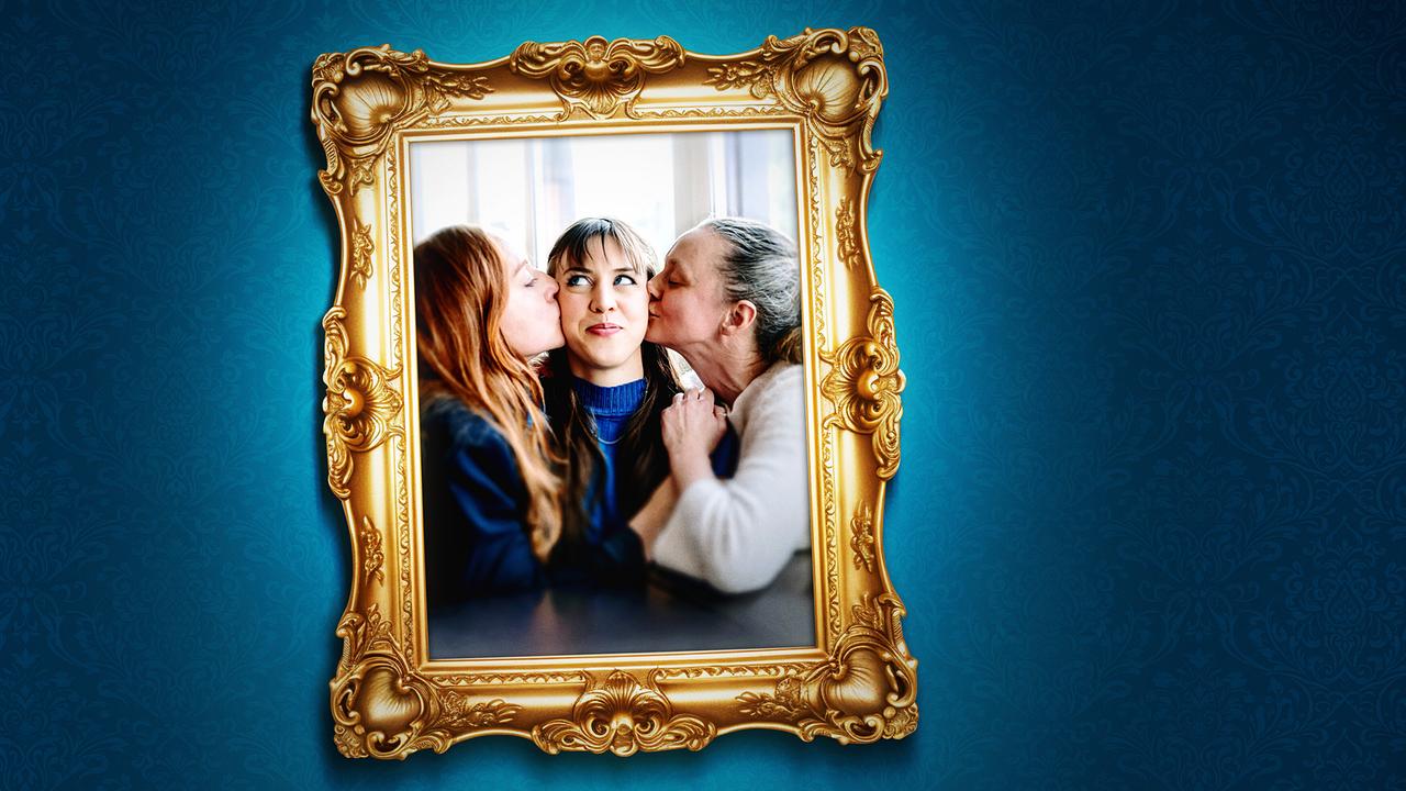 Ein gerahmtes Foto auf einer blauen Wand zeigt Balbina Augustin und Inka Schaller, die Hedwig Schaller in der Mitte einen Kuss auf die Wange geben.