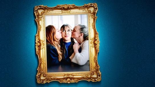 Ein gerahmtes Foto auf einer blauen Wand zeigt Balbina Augustin und Inka Schaller, die Hedwig Schaller in der Mitte einen Kuss auf die Wange geben.