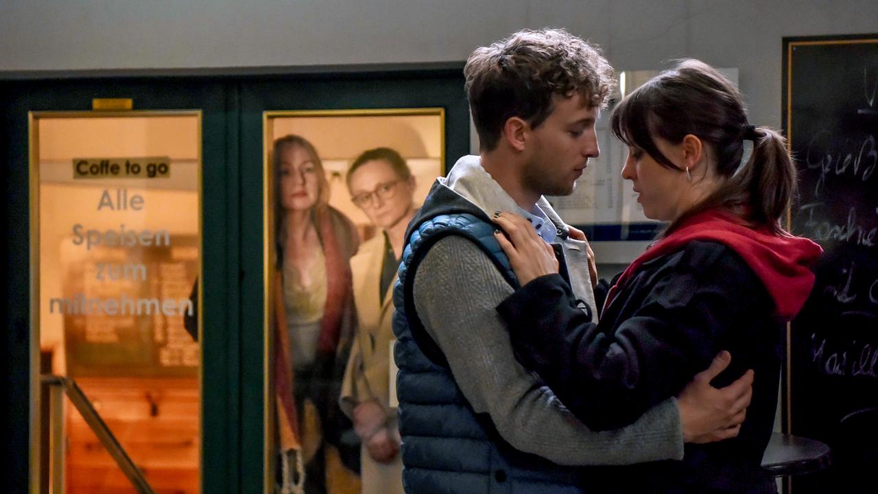 © ORF/BR/Cult Film/Hubert Mican Vor einem Beisl umarmen sich Andreas Hofer und Hedwig Schaller eng, während im Hintergrund durch eine Glastür Balbina Augustin und Inka Schaller zuschauen.