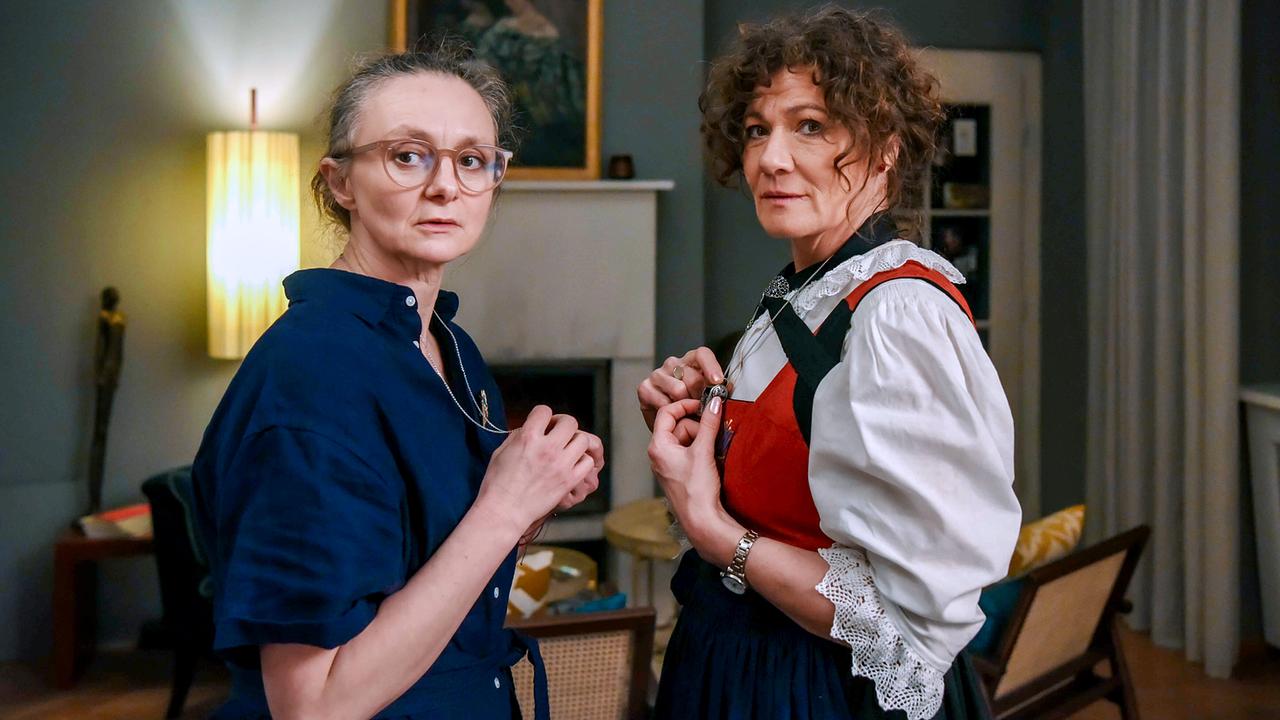 © ORF/BR/Cult Film/Hubert Mican Inka Schaller und Petra Hofer in Tracht stehen sich im Wohnzimmer gegenüber und blicken in eine Richtung.