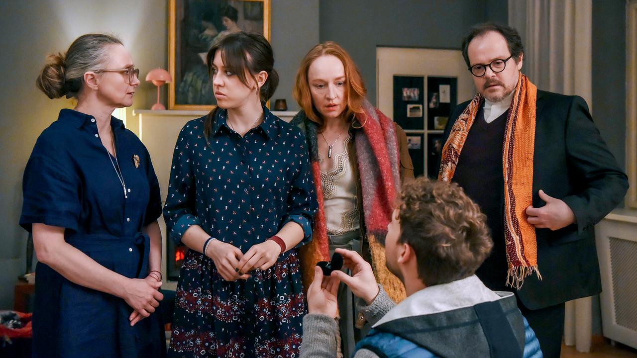 © ORF/BR/Cult Film/Hubert Mican Im Wohnzimmer kniet Andreas Hofer vor Hedwig Schaller und hält ein kleines Etui mit einem Ring hoch, während Inka Schaller, Balbina Augustin und Edgar neben Hedwig stehen.