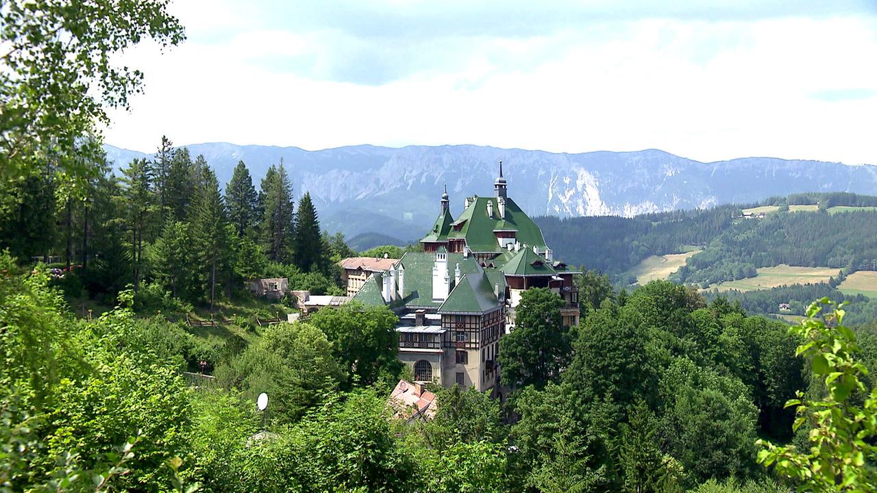 © ORF/Landesstudio Niederösterreich Das SüdbahnHotel Semmering mit grünen Dächern liegt eingebettet in einer bewaldeten Berglandschaft mit Alpenpanorama.