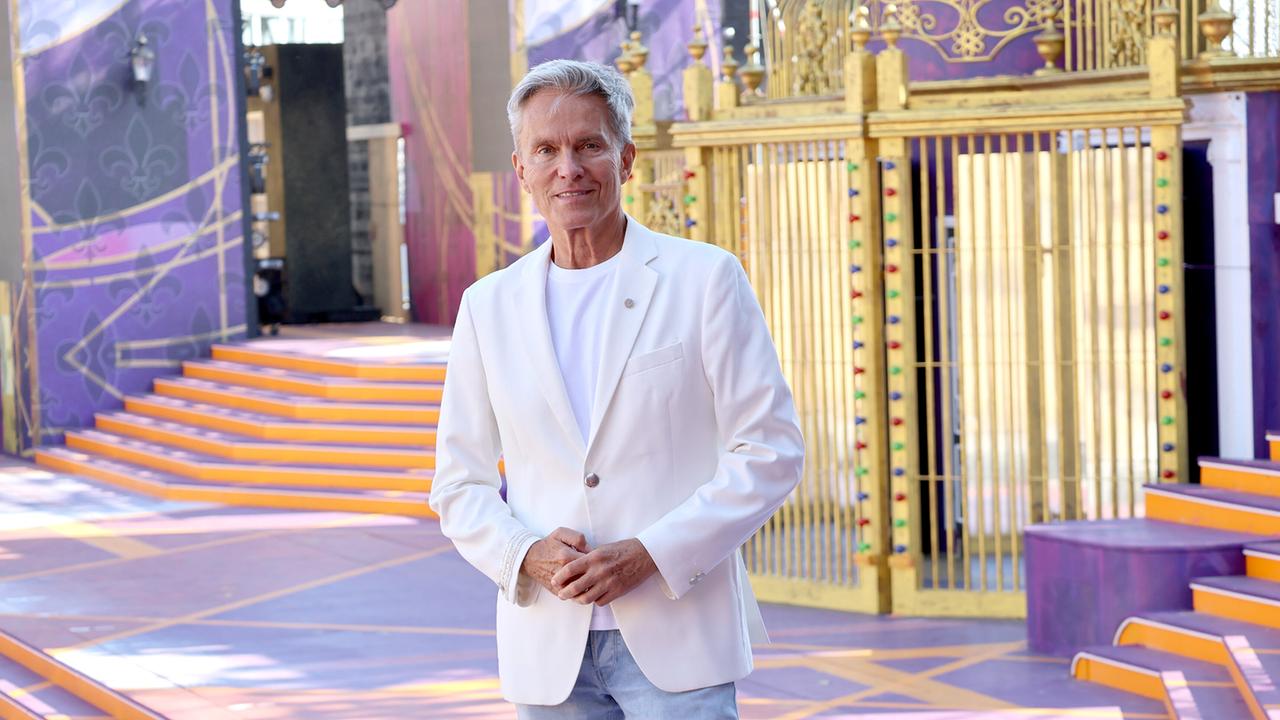 © ORF/Landesstudio Burgenland/Markus Fuchs Moderator Alfons Haider steht in einem farbenprächtigen, bühnenartigen Ambiente mit goldenen und violetten Dekorationen auf der Bühne von „Ein Käfig voller Narren“ auf der Seebühne Mörbisch