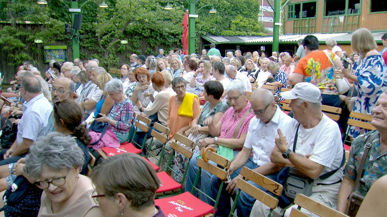 © ORF/Landesstudio Wien Zahlreiche Besucherinnen und Besucher sitzen dicht gedrängt im begrünten Innenhof vor einer Veranstaltung in der Tschauner Bühne.