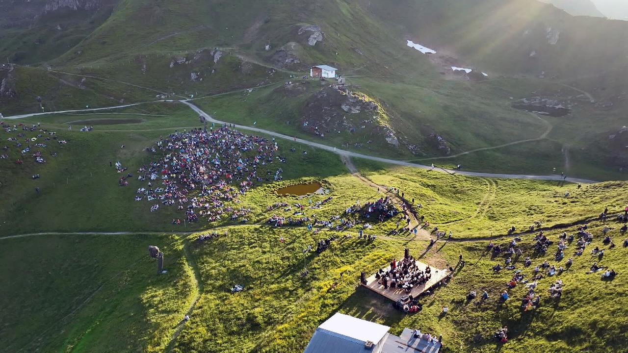 In einer alpinen Landschaft verfolgt ein weit verstreutes Publikum ein Konzert auf der Bühne Gasteinertal mitten auf einer Bergwiese.