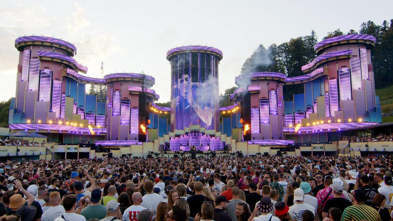 Eine große Menschenmenge feiert vor einer spektakulär beleuchteten Festivalbühne mit türkis- und violettfarbenen Türmen beim Electric Love Festival.