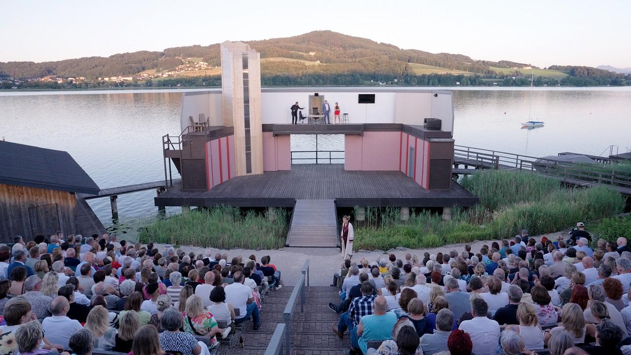 Vor der Kulisse eines Sees findet eine Aufführung auf der großzügigen Seebühne Seeham vor dicht besetzten Zuschauerreihen statt.